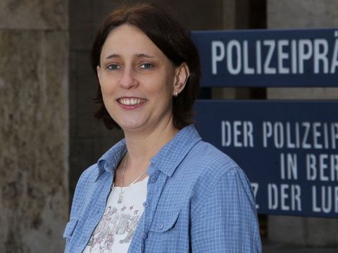 Eine Kriminalpolizistin trägt eine blaue Bluse und lächelt in die Kamera.